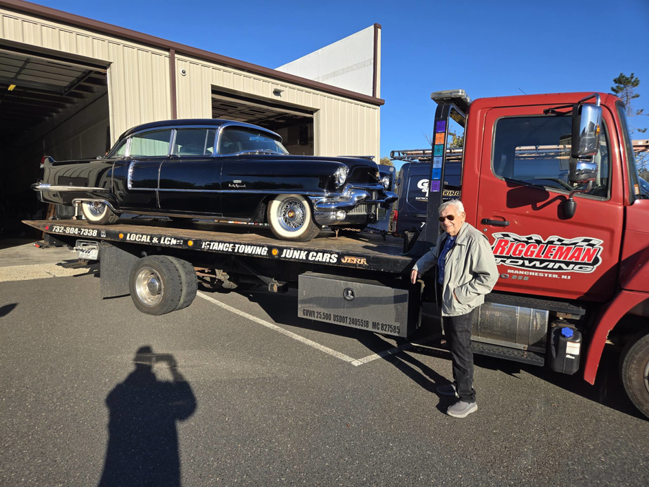 A classic black car being transported on a flatbed tow truck by Riggleman Towing in Moorefield, WV.