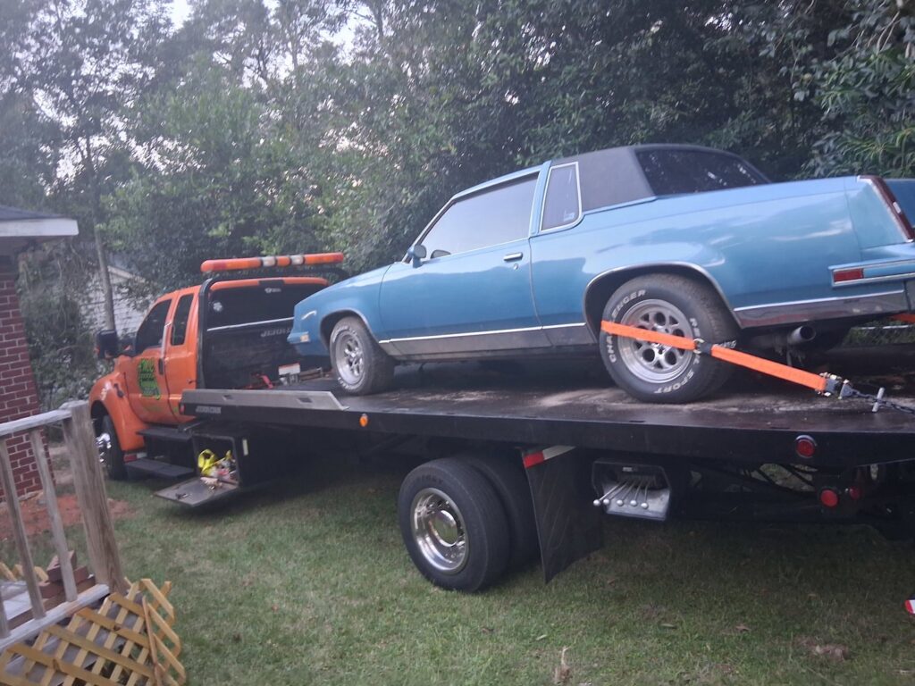A blue classic car being transported on a flatbed tow truck by AMC Towing in Mobile, AL.