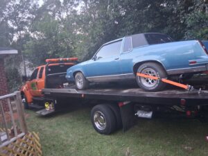 A blue classic car being transported on a flatbed tow truck by AMC Towing in Mobile, AL.