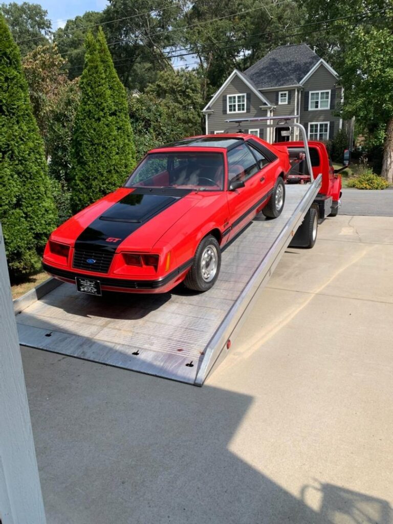 A classic red and black Ford Mustang being loaded onto a flatbed tow truck by Acme Towing Services in Greenville, SC.