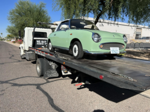 A classic light green car being transported on a flatbed tow truck by Trejo's Towing LLC in Phoenix, AZ.