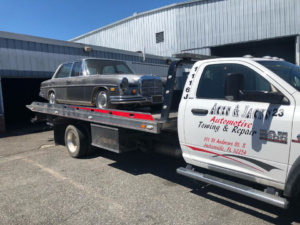 A classic Mercedes-Benz sedan being towed on a flatbed truck by Aces & Jacks Automotive in Jacksonville, FL.