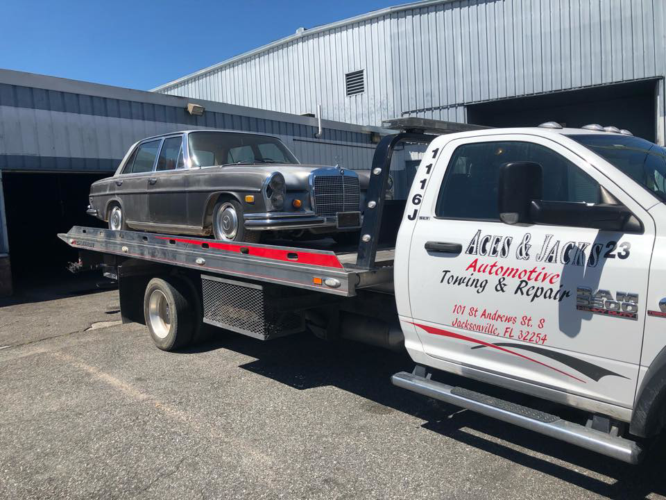A classic Mercedes-Benz sedan being towed on a flatbed truck by Aces & Jacks Automotive in Jacksonville, FL.