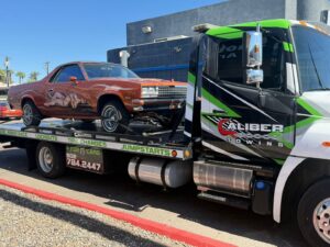 A classic orange El Camino being transported on a flatbed tow truck by Caliber Towing in Phoenix, AZ.