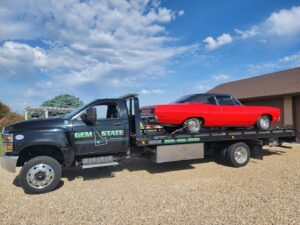 A classic red car being transported on a flatbed tow truck by Gem State Towing and Recovery in Caldwell, ID.