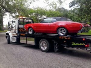 A classic red convertible car loaded onto a white flatbed tow truck from Glenn's Towing & Recovery Inc in Lafayette, LA.