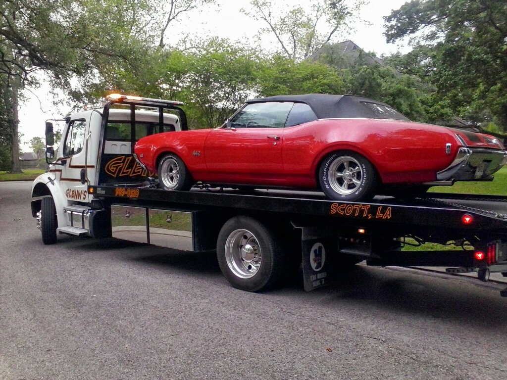 A classic red convertible car loaded onto a white flatbed tow truck from Glenn's Towing & Recovery Inc in Lafayette, LA.