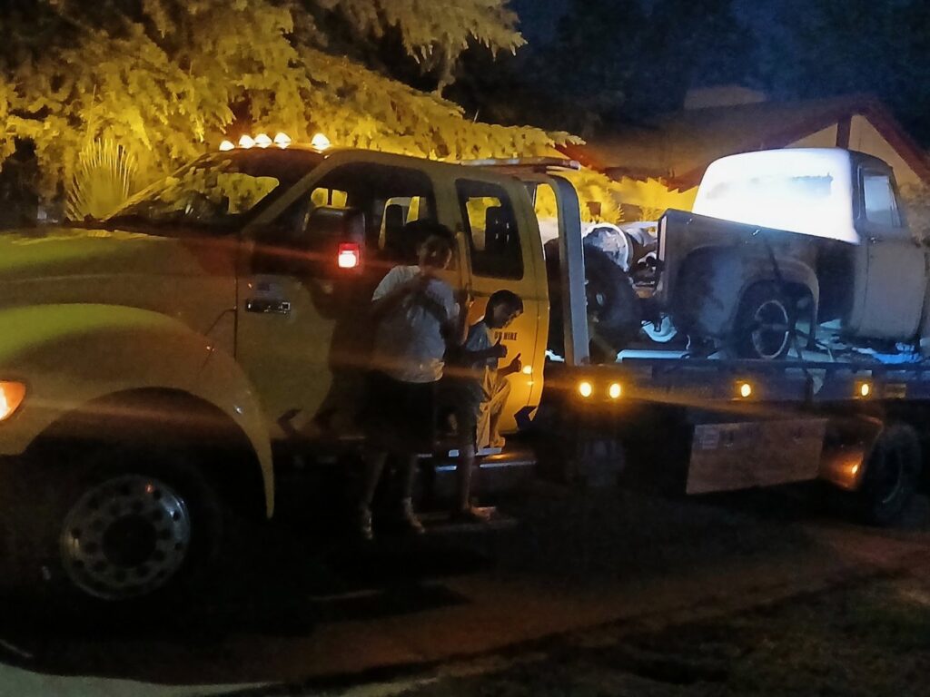 An older model truck being transported on a yellow flatbed tow truck by A&A Towing Services in Bakersfield, CA.