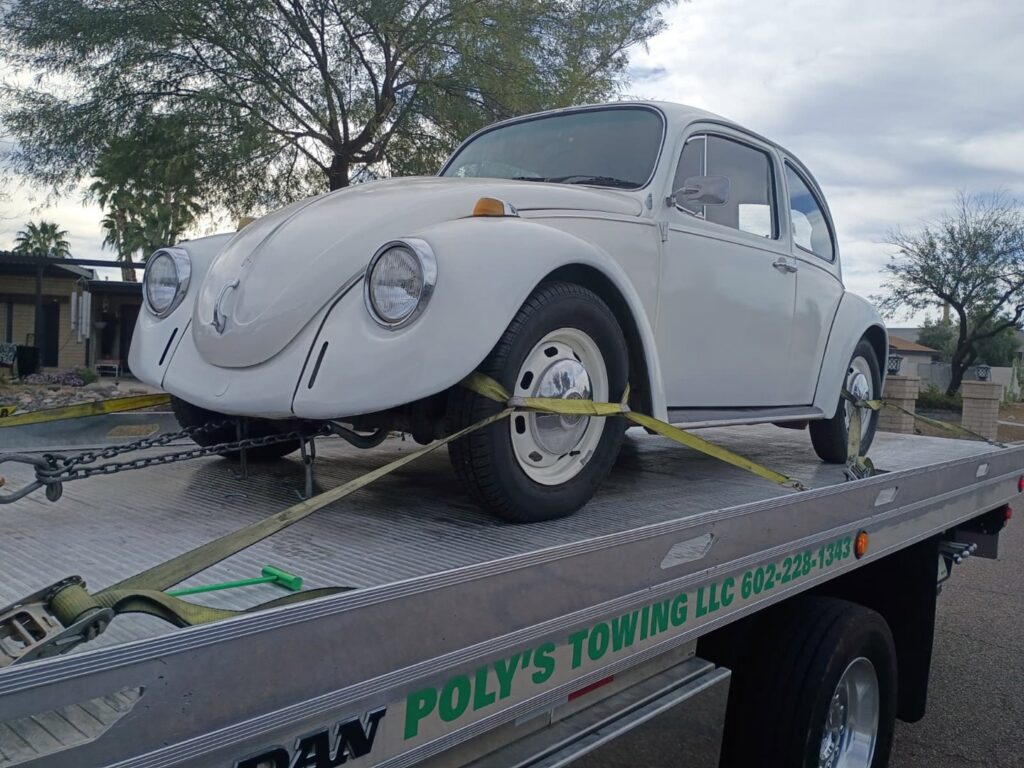A white classic Volkswagen Beetle loaded on a flatbed tow truck by Poly's Towing Glendale in Glendale, AZ.