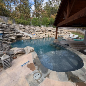 A sparkling clean backyard pool with rock features and a cleaning brush, maintained by AW Pool Service in Tulsa, OK.