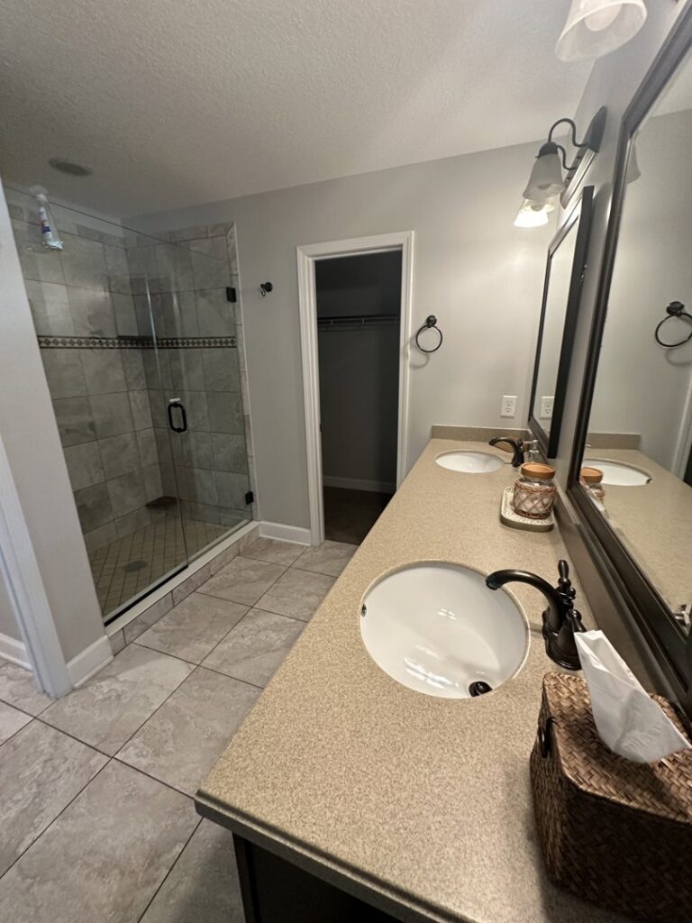A clean bathroom featuring a double vanity and a modern glass shower, showcasing the quality cleaning by CLEAN That SHEET LLC in Jacksonville, FL.