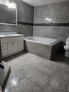 A spotless bathroom with grey tiled walls and floor, featuring a clean bathtub and vanity, cleaned by Way Too Bright Services LLC in Rockford, IL.
