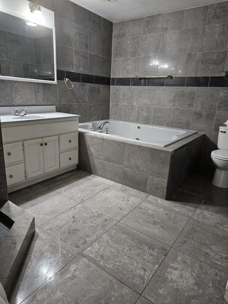 A spotless bathroom with grey tiled walls and floor, featuring a clean bathtub and vanity, cleaned by Way Too Bright Services LLC in Rockford, IL.