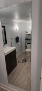 A clean bathroom mirror reflecting a tidy bathroom with a cleaning tool on the floor, indicating professional service from Nichelle's touch housekeeping LLC in Detroit, MI.