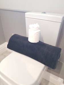 A sparkling clean toilet with a neatly folded towel and decorative toilet paper, showcasing a finished bathroom by Pretty & Polished Cleaning Services in Sandy, OR.