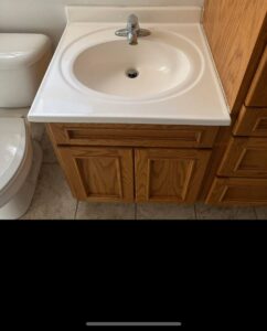 A clean bathroom vanity with a white sink and wooden cabinets after professional cleaning by Teri Lynn's Cleaning in Williston, ND.