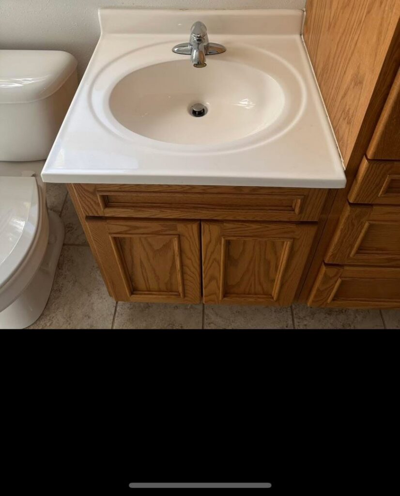 A clean bathroom vanity with a white sink and wooden cabinets after professional cleaning by Teri Lynn's Cleaning in Williston, ND.