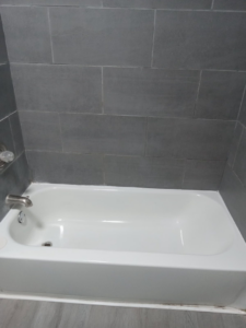 A sparkling clean bathtub with modern grey tiled walls, showcasing the quality house cleaning services by Dacari's Helping Hands LLC in South Bend, IN.