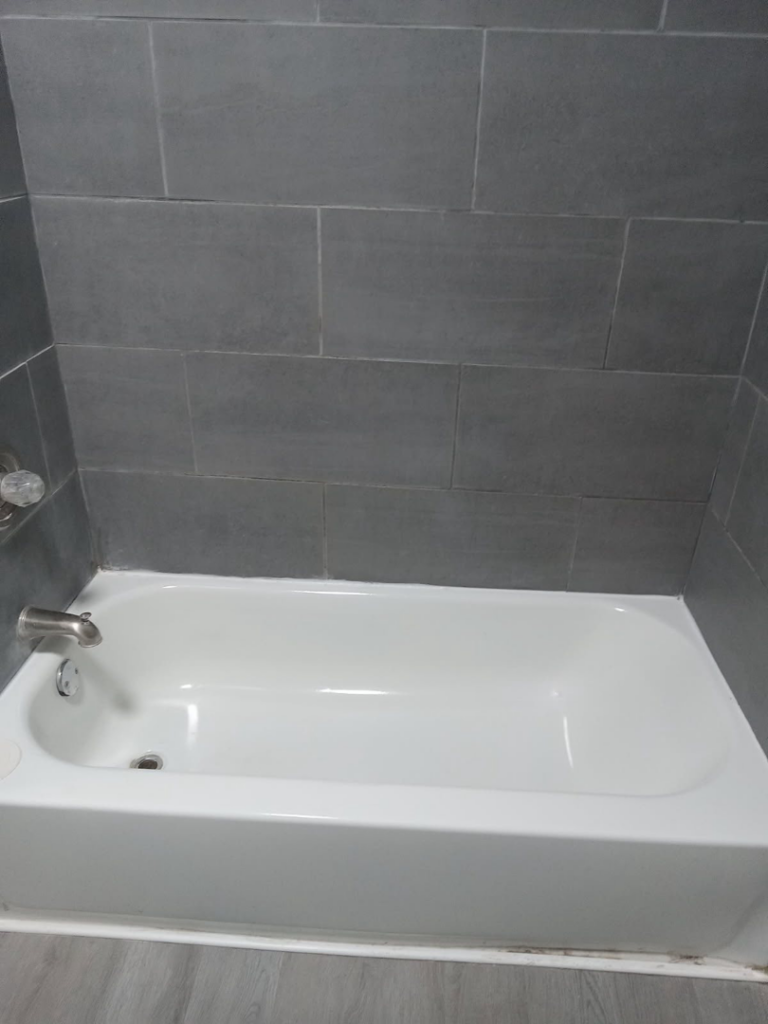 A sparkling clean bathtub with modern grey tiled walls, showcasing the quality house cleaning services by Dacari's Helping Hands LLC in South Bend, IN.