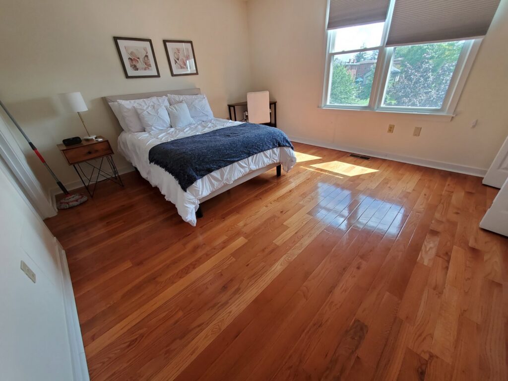 A freshly cleaned bedroom with shiny wood floors and a mop visible, showcasing the work of Maids of Hartford in Hartford, CT.