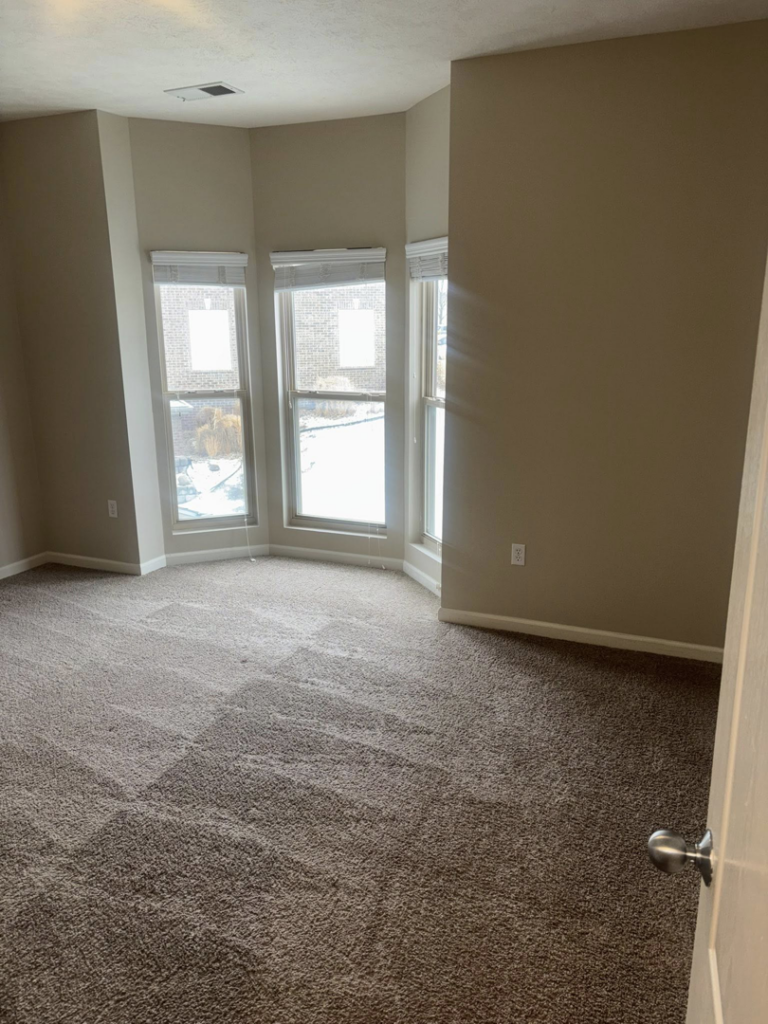 A clean, empty bedroom featuring bay windows and freshly vacuumed carpet, demonstrating move-out cleaning by NACleaning Co. in Omaha, NE.