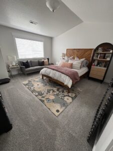 A neatly cleaned bedroom featuring a bed, grey sofa, and floral rug, showcasing Kleen Slate's cleaning in Shakopee, MN.