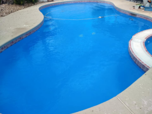 A clean, blue swimming pool with a pool vacuum hose for maintenance by Bluemar Pool & Spa Services in North Las Vegas, NV.