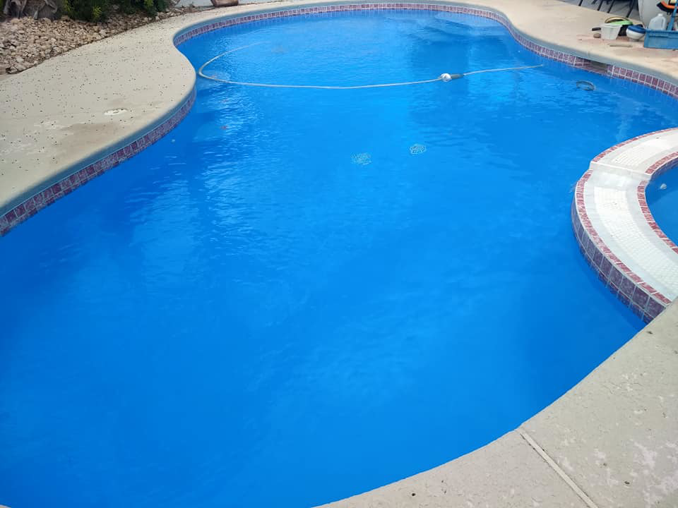 A clean, blue swimming pool with a pool vacuum hose for maintenance by Bluemar Pool & Spa Services in North Las Vegas, NV.