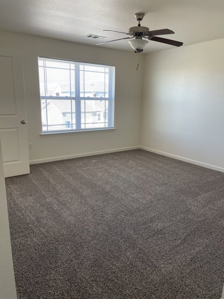 A clean, empty bedroom with plush carpet and ceiling fan, professionally cleaned by 307 Maid in Cheyenne, WY.