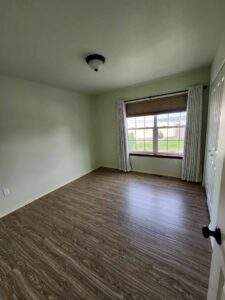 A clean and empty bedroom with light green walls and wood-look flooring, ready for occupancy after cleaning by E-N-S Home Cleaning Solutions, LLC in Lewiston, ID.