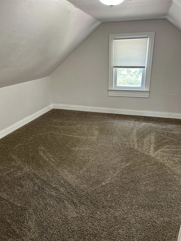 A clean, empty room with freshly vacuumed carpet and a window, showcasing the quality work by Genesis Cleaning Services in Raleigh, NC.