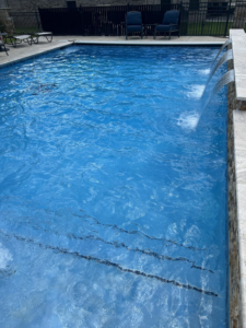 A beautifully clean in-ground pool with a decorative waterfall feature, maintained by Pips Pool Service in Enid, OK.