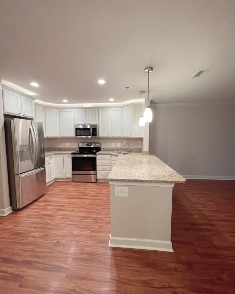 A sparkling clean kitchen with white cabinets, stainless steel appliances, and hardwood floors after a professional house cleaning by Rivas Molina's Cleaning LLC in Dundalk, MD.