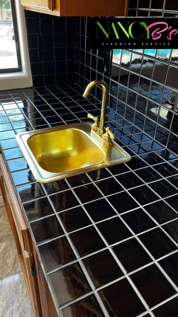 A clean kitchen counter with black tiles and a polished brass sink by Nancy B's Cleaning Service LLC in Atlanta, GA.