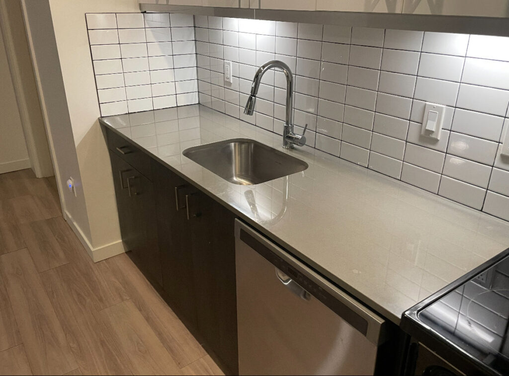 A sparkling clean kitchen countertop with a sink and dishwasher, showcasing the quality work of Merriweather Cleaning and Laundry in Vancouver, WA.