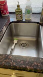 A sparkling clean kitchen sink with a brush and soap bottles, showcasing the results of Picky Performance Cleaning in North Las Vegas, NV