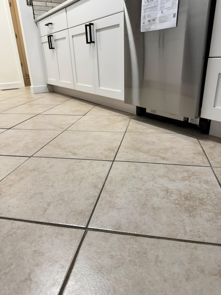 A close-up of a clean kitchen tile floor with sparkling grout, cleaned by Dust Detail Cleaning Services in Post Falls, ID.