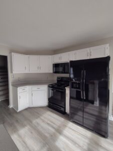A clean kitchen featuring white cabinets, black appliances, and light wood floors, cleaned by Tessa's Cleaning Service in Chesapeake, VA.