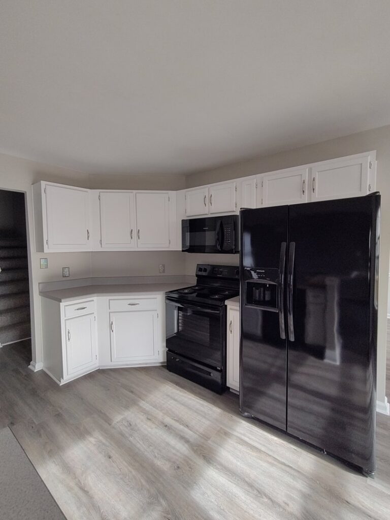 A clean kitchen featuring white cabinets, black appliances, and light wood floors, cleaned by Tessa's Cleaning Service in Chesapeake, VA.