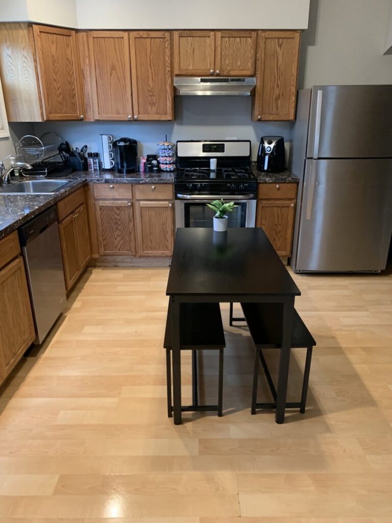 A clean kitchen with wooden cabinets, stainless steel appliances, and a dining table, showcasing the results of Faye Cleaning Service LLC in Ankeny, IA.