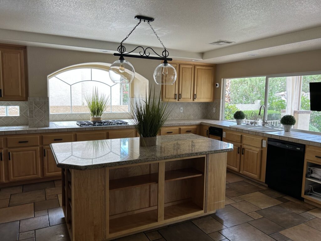 A clean kitchen with light wooden cabinets, granite countertops, and a central island, showcasing cleaning by JG Clean Solutions in Henderson, NV.