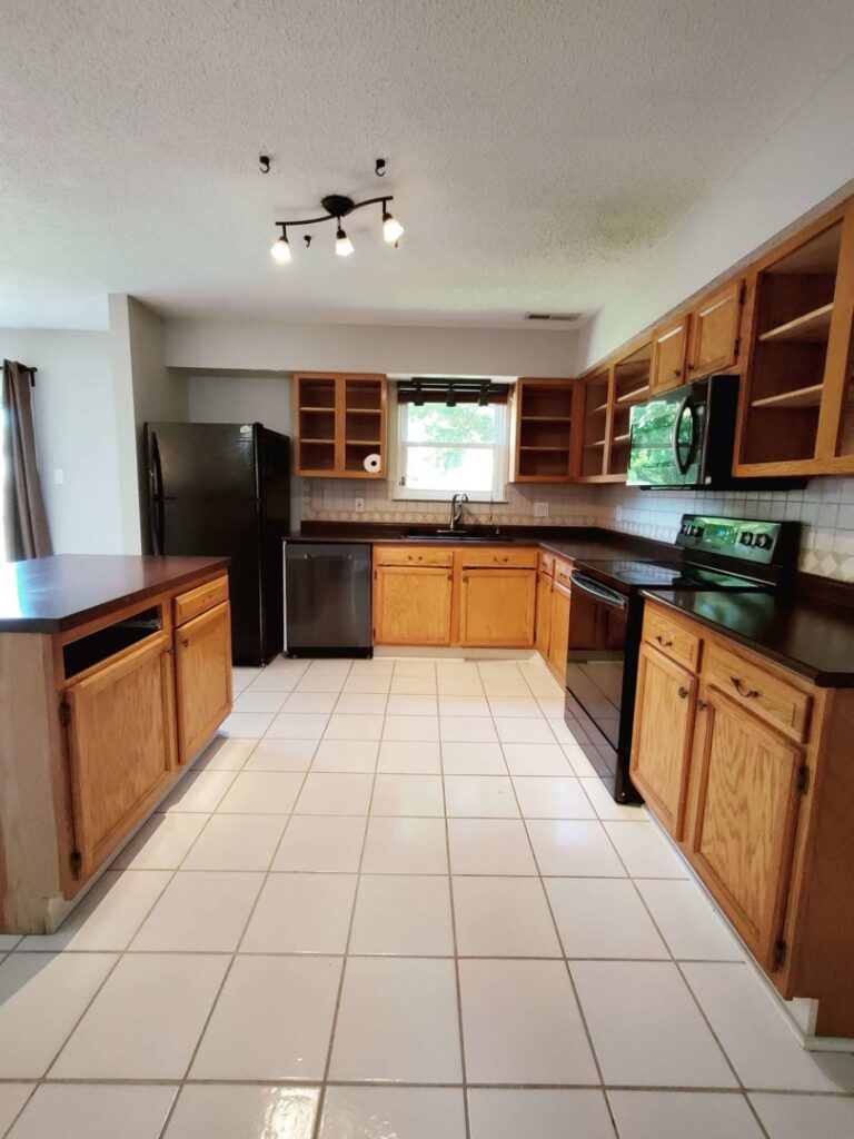 A clean kitchen with light wood cabinets, black appliances, and white tiled floors, cleaned by Tessa's Cleaning Service in Chesapeake, VA.