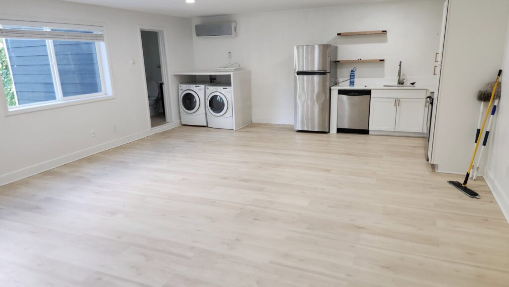 A spacious, clean room featuring a laundry area, kitchen appliances, and light wood floors, cleaned by Eyedeal Cleaning Services in Gresham, OR.