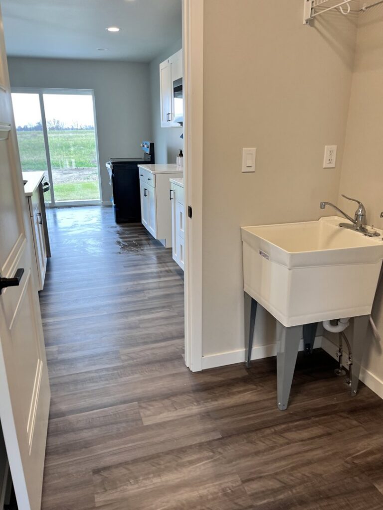 A freshly cleaned laundry and utility room featuring a sink and wet floor, indicating a professional cleaning service by Cedar Cleaners LLC in Cedar Rapids, IA.