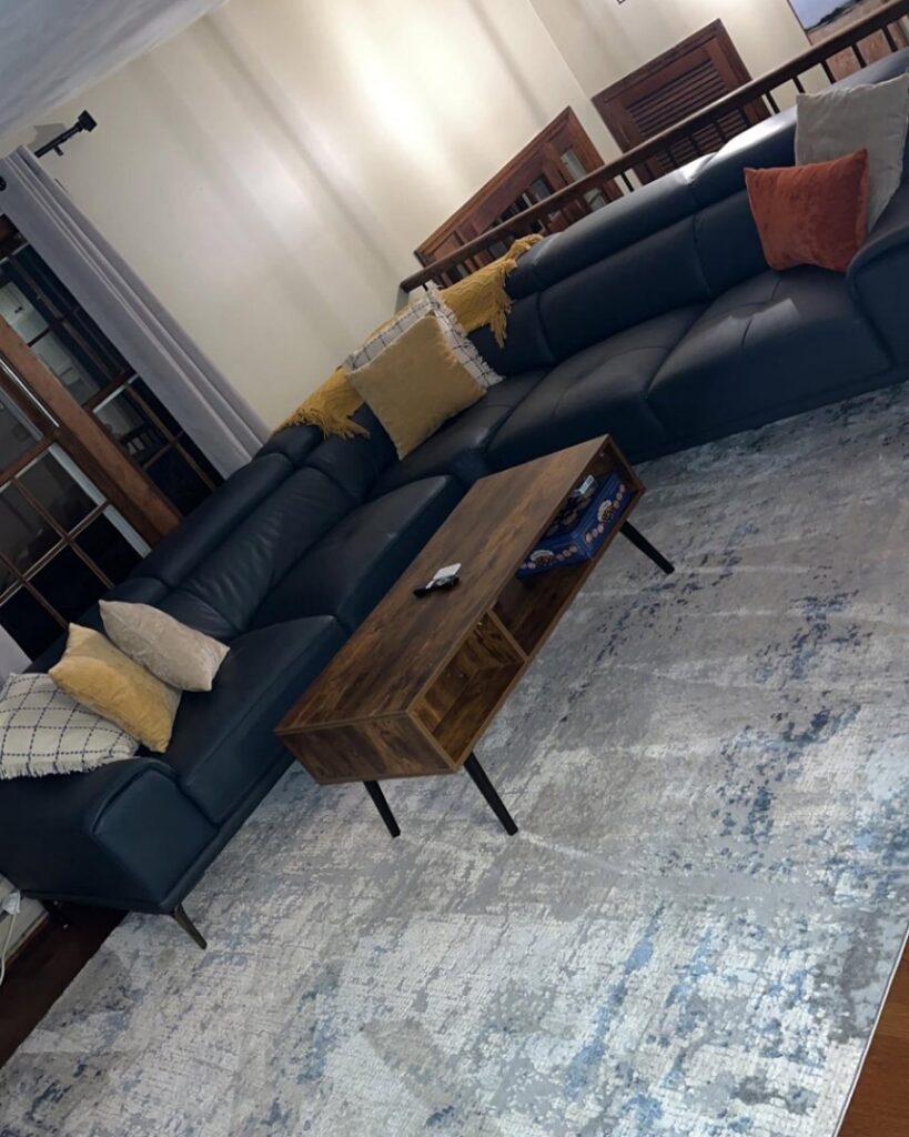 A clean and tidy living room featuring a large sectional sofa and a patterned rug, cleaned by Make It Shine in Worcester, MA