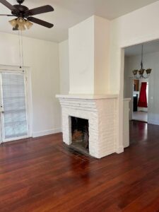 A clean living room featuring a white brick fireplace and polished hardwood floors by Nannie Needs LLC in Kent, WA.