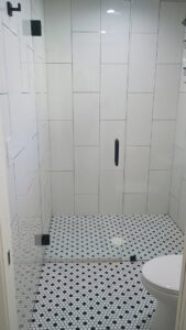 A modern and impeccably clean shower with white tiled walls and a stylish black and white patterned floor, cleaned by Carole's House Cleaning in Tempe, AZ.
