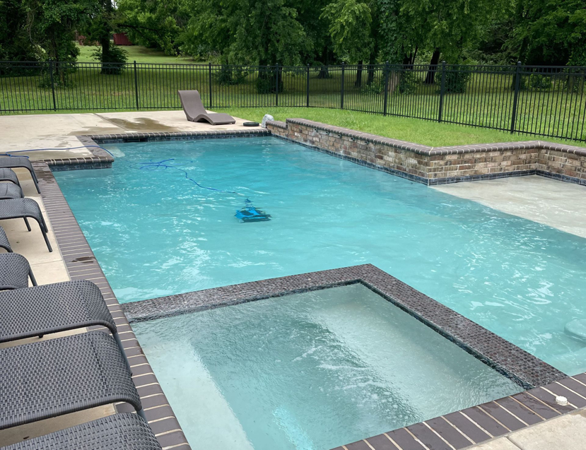 A pristine swimming pool with an attached spa and a robotic cleaner operating, serviced by AquaDocs in Dublin, OH.