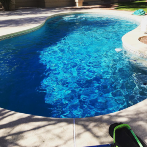 A sparkling clean pool with a pool cleaning hose and brush on the deck, maintained by Island pools in Scottsdale, AZ.