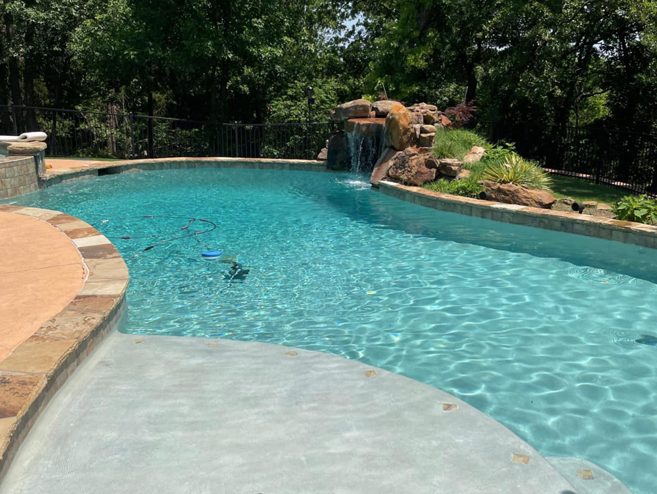 A sparkling clean pool with a rock waterfall and a robotic cleaner in the water by AquaDocs in Dublin, OH.
